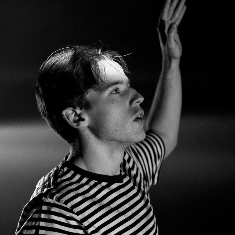 Black and white photo of Paul dancing in a striped top with one arm raised up