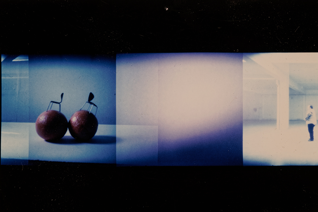 A photo that is split screen in one side are two oranges with small wire chair designs stuck into the fruit, and in the last third a dancer stands looking forward